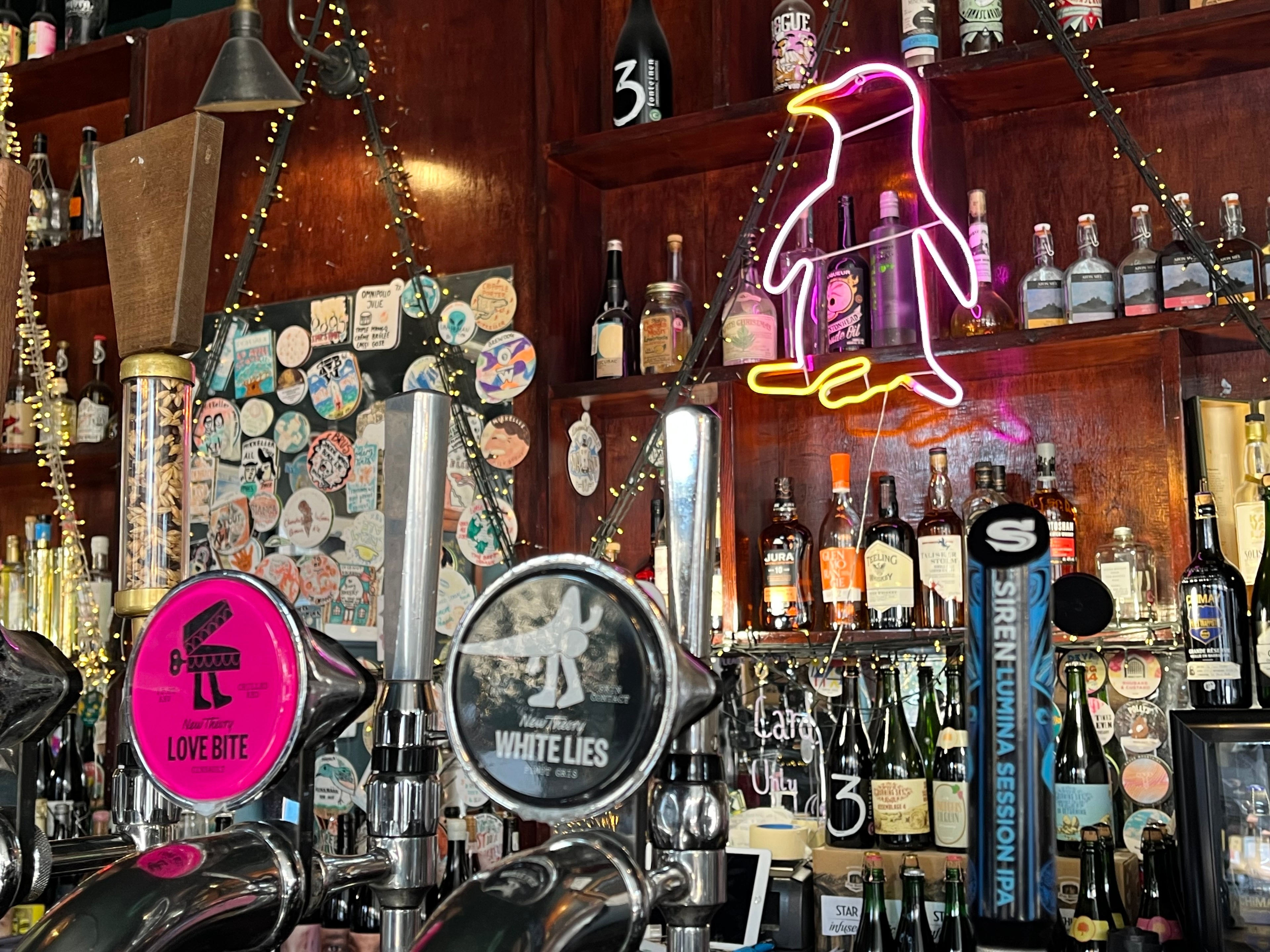 Neon penguin sign above a bar with various bottles and beer taps.